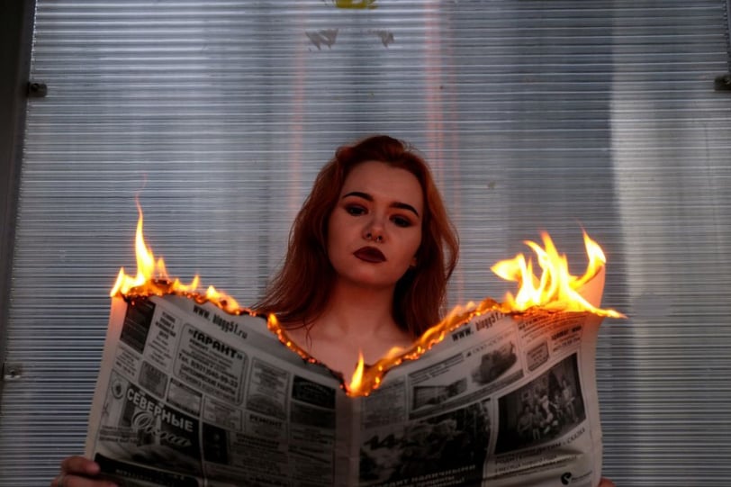 Woman holding a newspaper that is on fire.