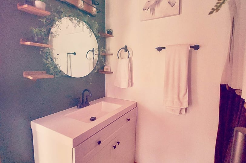 a bathroom with a round mirror and wooden shelves and black hardware hunter green and white