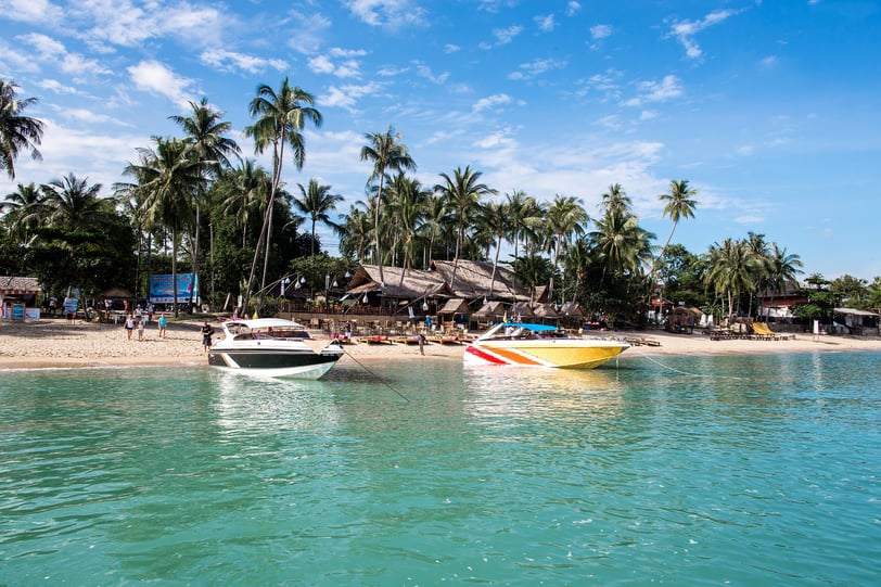 A picturesque beach in Koh Samui, Thailand, with two speedboats docked on the shore and palm trees