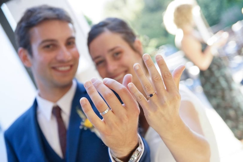 Photo de coule de jeunes mariés montrant leurs alliances avec le sourire.