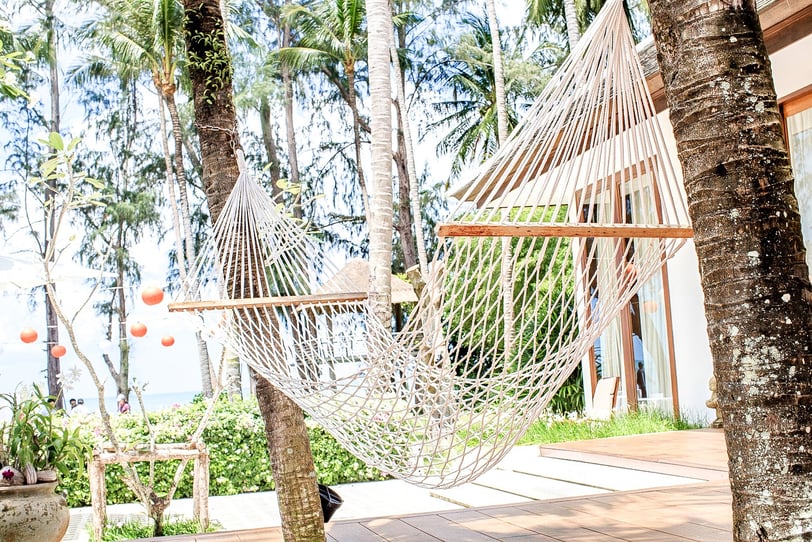 **Alt-Text:**  A white rope hammock hanging between two palm trees in a tropical garden on Koh Samui