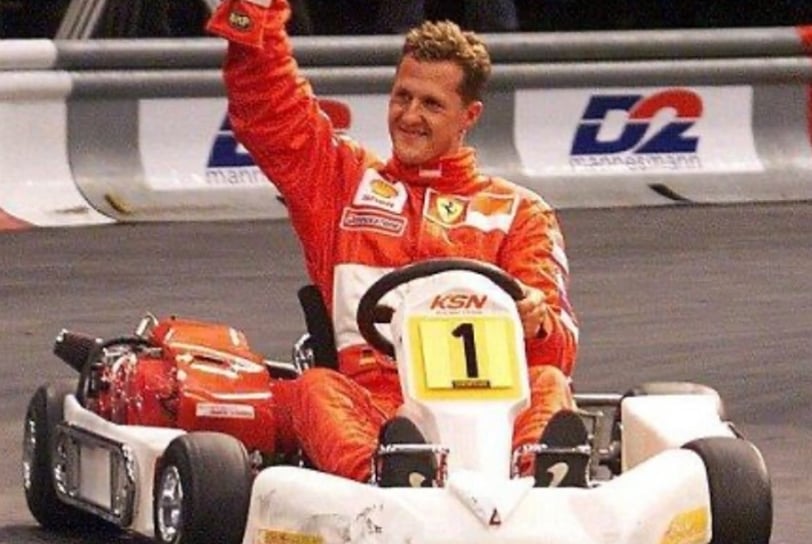 Pilote en tenue Ferrari saluant avec un casque en main dans un kart blanc marqué "KSN"