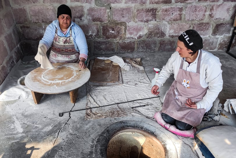 women baking traditional lavash bread in clay oven