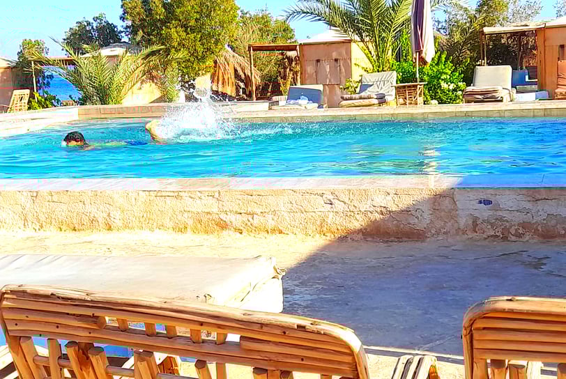 Menino nadando na piscina perto do mar e bangalô na estrela beduína Egito