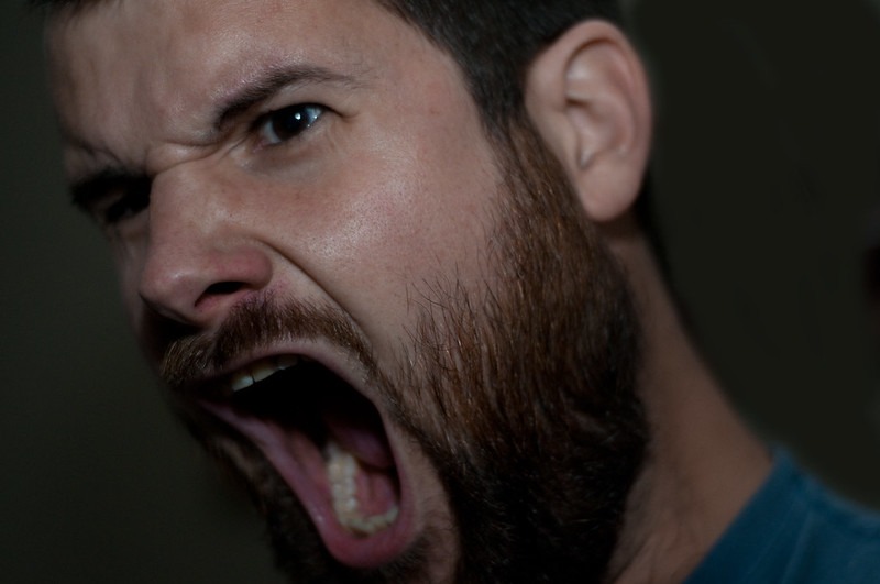 Man with a beard has his mouth wide open and is screaming