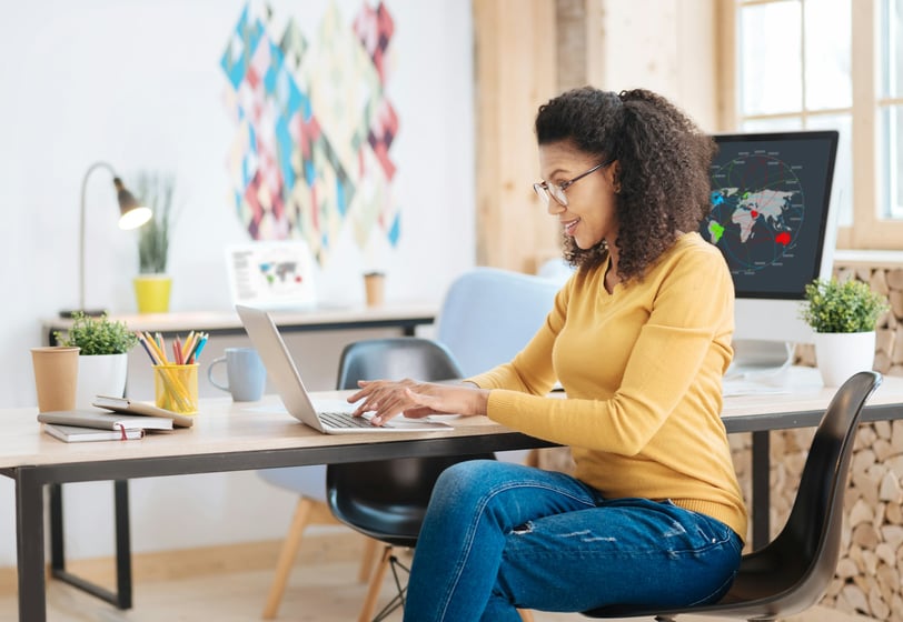 a woman wearing a m sweater and jeans, sitting at a desk working on a laptop computer