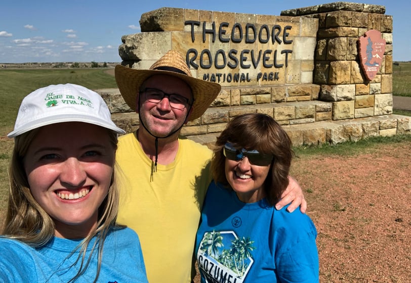 a man and two women standing in front of a sign that says theodore roosevelt national park