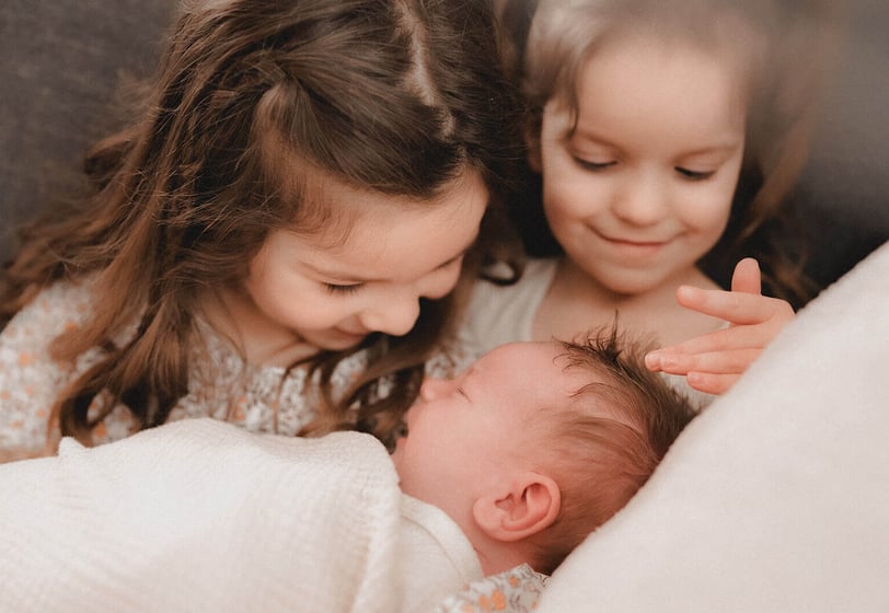 Two sisters holding new baby brother and feeling baby's hair