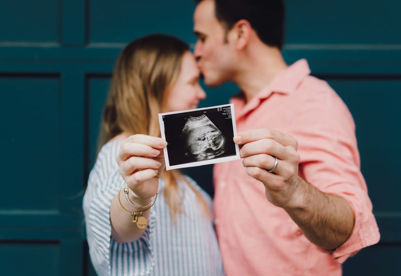 a pregnant woman and her husband kissing in front of a blue wall