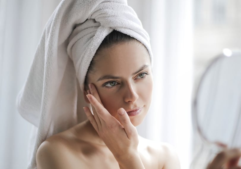 a woman with a towel wrapped around her head looking in a hand held mirror