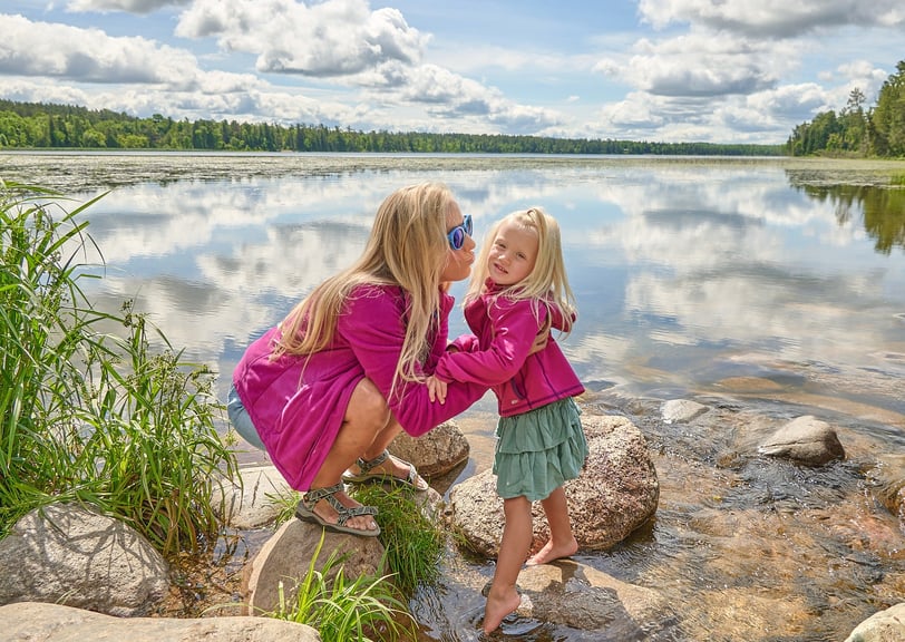 a mother and her girl in pink jackets standing in front of a lake