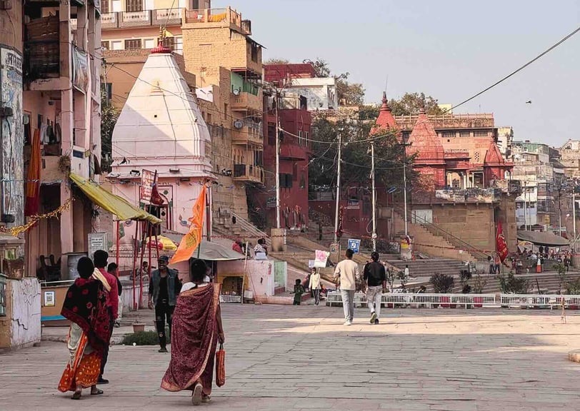 Two people walking along the ghats of Varanasi, India, by the Ganges River.