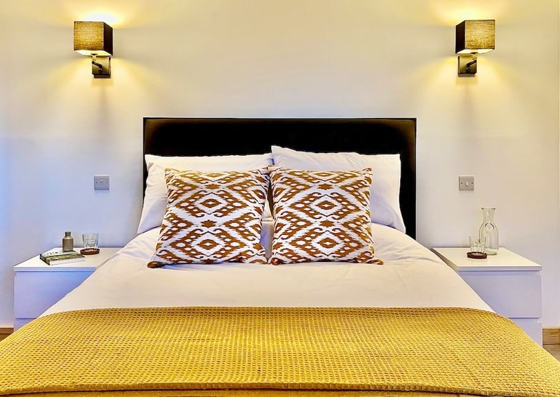 a large bed with wall lights and colourful cushions and throw