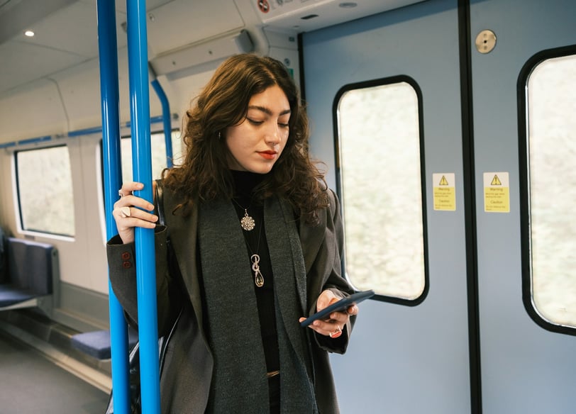 A woman standing in a train car, looking at her smartphone