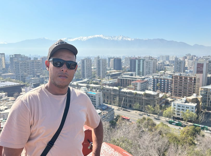 uma pessoa de óculos escuro de costa para a cidade e no fundo as cordilheiras dos andes no chile