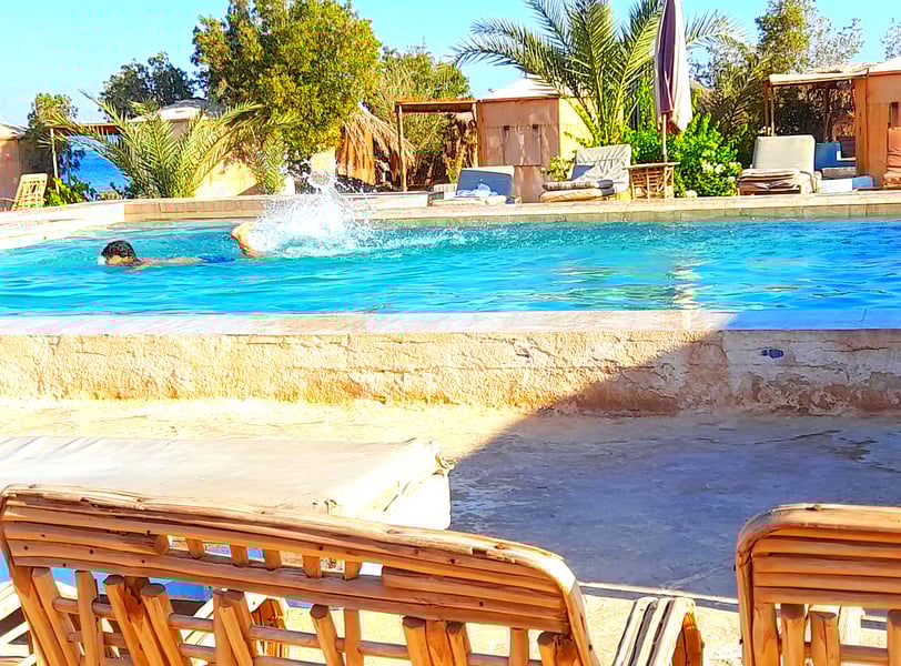 Pojke simmar i poolen nära havet och bungalow på beduinstjärnan Egypten