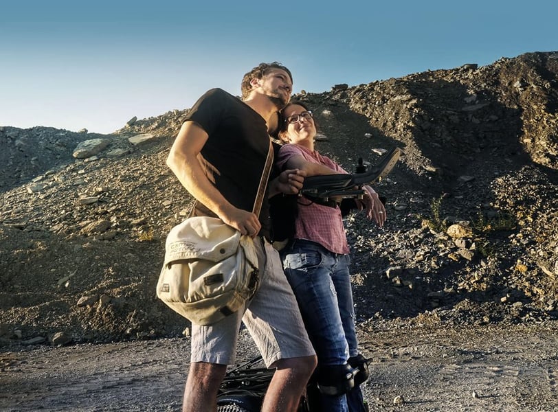 a man and woman in a standing wheelchair standing in front of a mountain