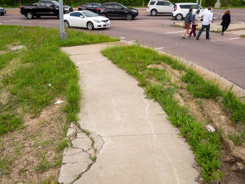 Photo of a cracked up sidewalk leading to a busy intersection