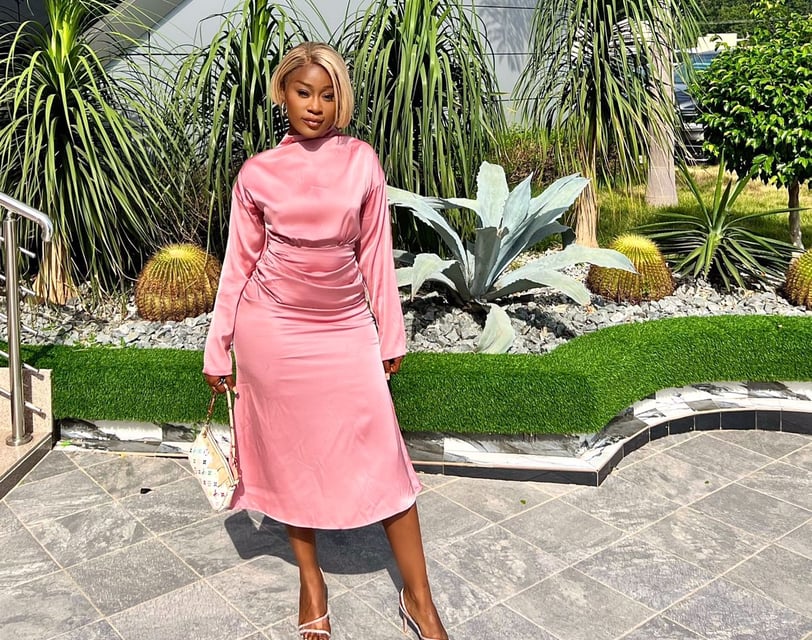 Efia Odo in a pink overall dress with a designer handbag.