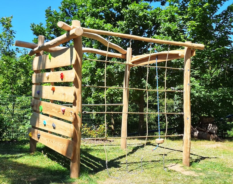 Spielplatz aus robustem Holz mit Klettergriffen, Kletternetz, Schaukel und Reckstange
