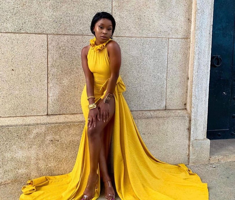 Efia Odo posed by a wall in a stunning yellow overall dress.