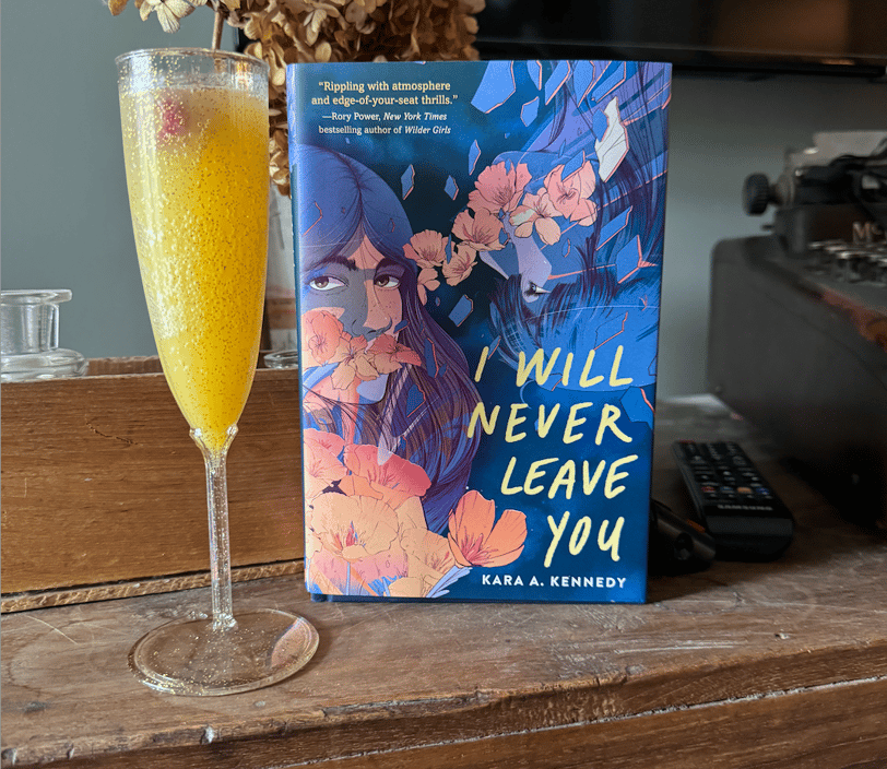 A hardcover copy Kara A. Kennedy's novel I WILL NEVER LEAVE YOU standing next to a mimosa glass