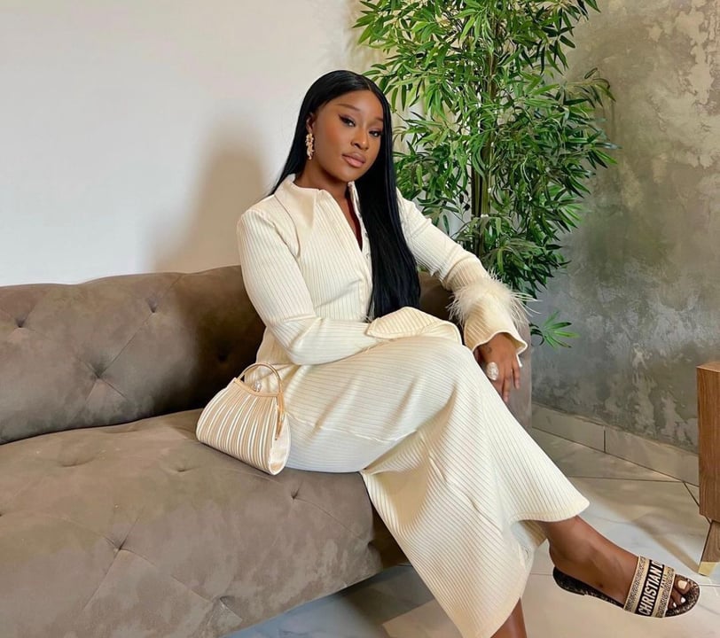 Efia Odo sitting on a couch dressed in a matching dress with a bag.