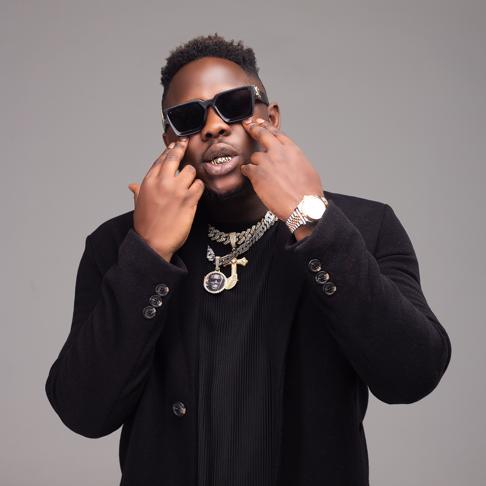 Medikal in sunglasses with chains on his neck.