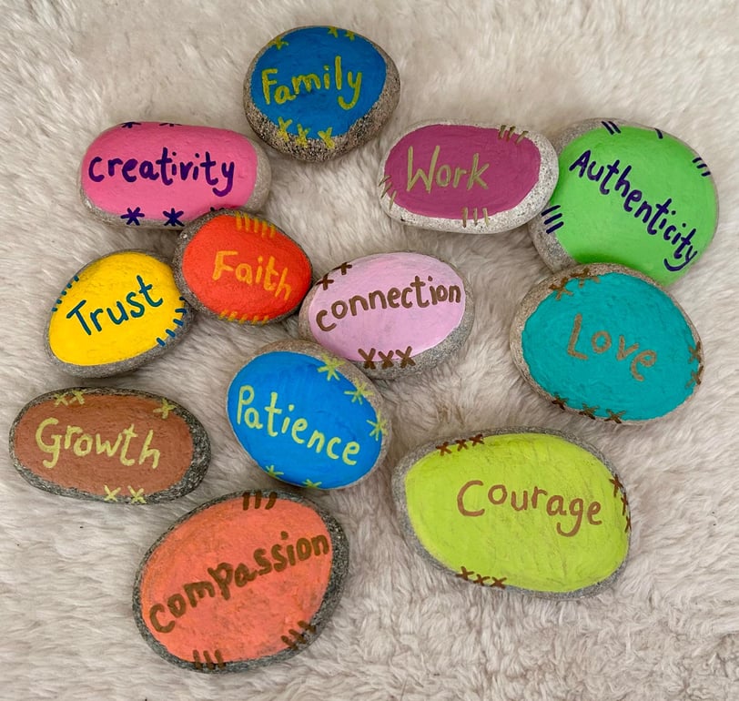 Therapy stones with values words painted on colourful backgrounds, placed on a furry surface.