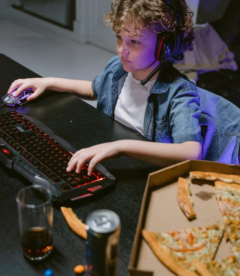 Child playing games on laptop, listening to music and eating fast food