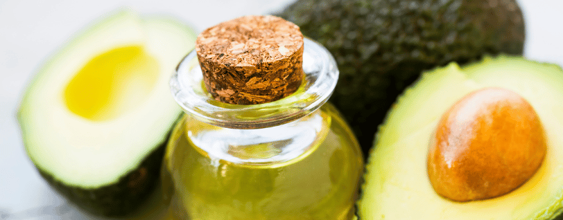 Une bouteille en verre avec l'huile d'avocat dedans et des avocats en fond