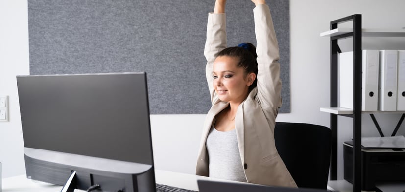 a woman sitting at a desk with her arms up in the air stretching