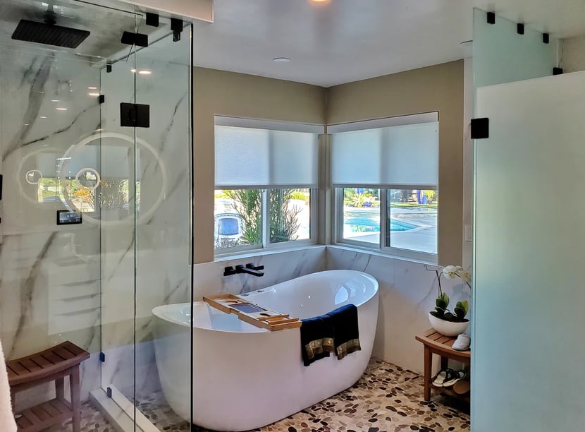 Elegant and bright master bathroom with marble wall, freestanding tub, and glass shower and toilet enclosures.