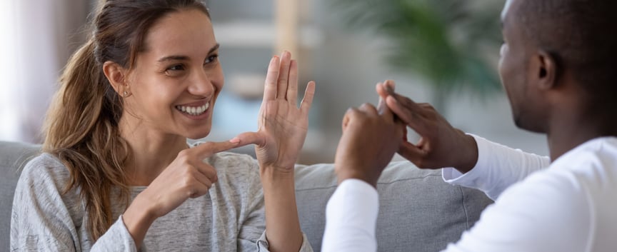 Image of a smiling woman and a man, signing together