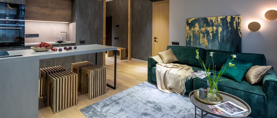 an open plan space with a emerald green sofa and coffee table and a kitchen island