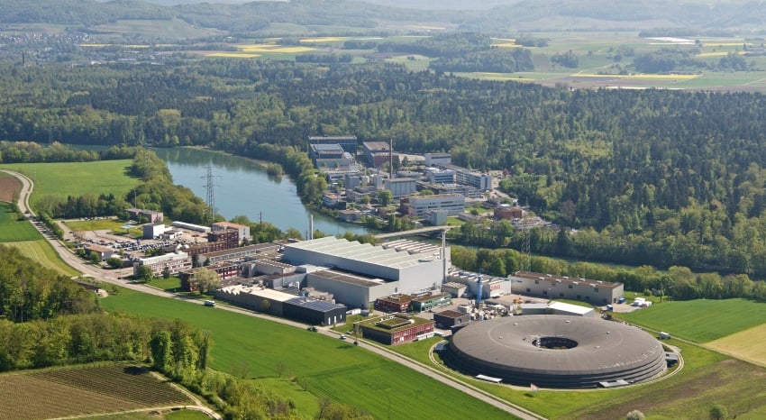Aerial view of Paul Scherrer Institute complex with verdant landscape, lake, and forested hills