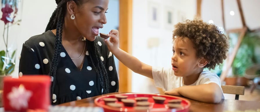 a black woman eating a snack from the hands of a black toddler with an afro