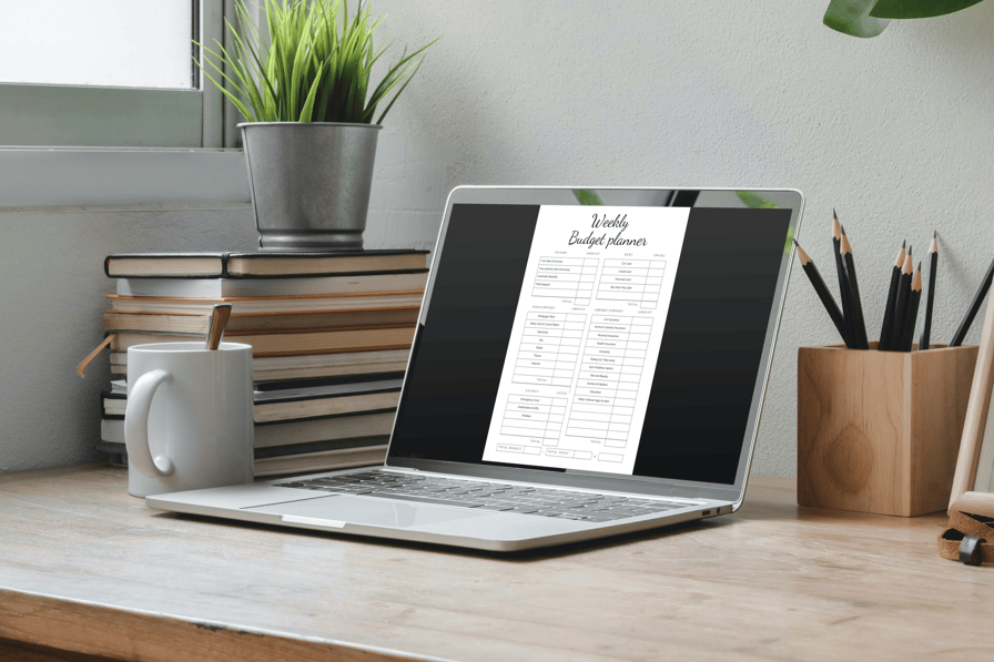 Weekly budget planner displayed on a laptop screen on a modern desk setup with books and plants