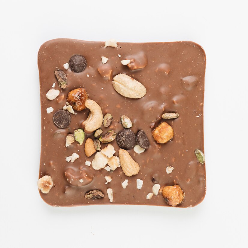 Top view of a milk chocolate square with nuts mixed in & on top like cashews, hazelnuts, pumpkin see