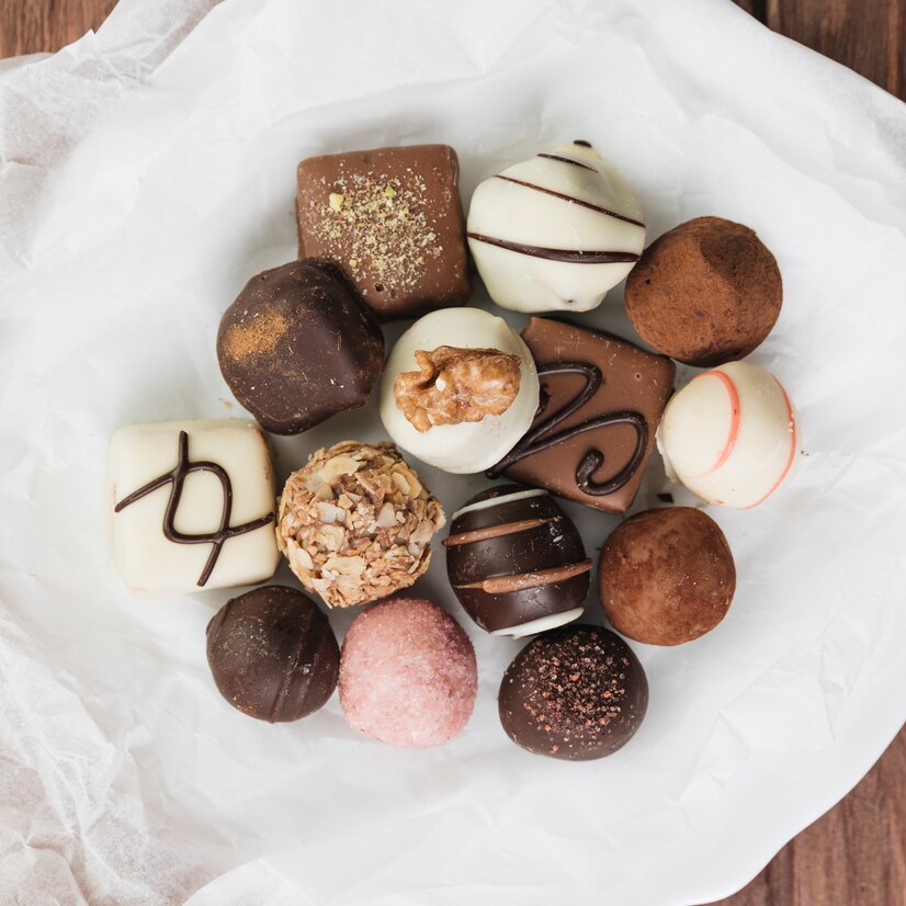 Top view of chocolates and truffles in white, milk, & dark varieties decorated with swirls & nuts