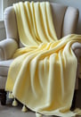 Light yellow waffle-knit throw with tassels on a beige armchair.
