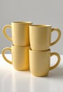Set of four stackable butter yellow mugs with rounded handles.