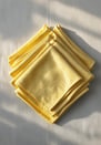 Neatly stacked butter yellow cloth napkins on a pale linen background.