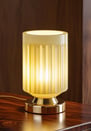 Soft yellow glass table lamp with a gold base, lit warmly against wood.