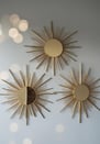 Set of three gold sunburst mirrors on a light grey wall.
