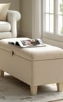 Light beige storage ottoman with textured fabric and wood legs, styled with an open magazine on top.