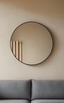 Round mirror with a thin black frame hanging above a modern grey couch.