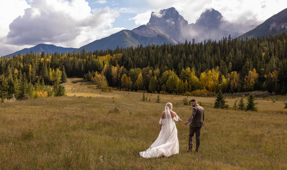 a bride and groom walking through a field in Canmore