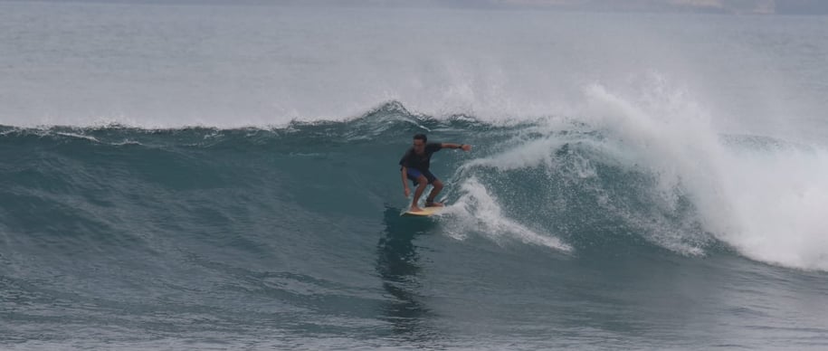 Romi riding a wave while surfing at Ekas beach, showcasing his skills as an experienced instructor.