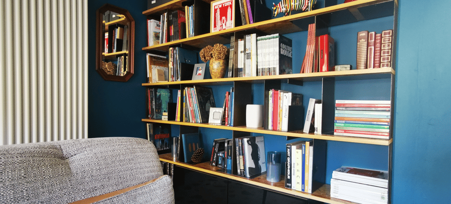 Bibliothèque sur mesure aménagée dans une niche bleue dans le salon TV. Étagères OSB, support tôle.